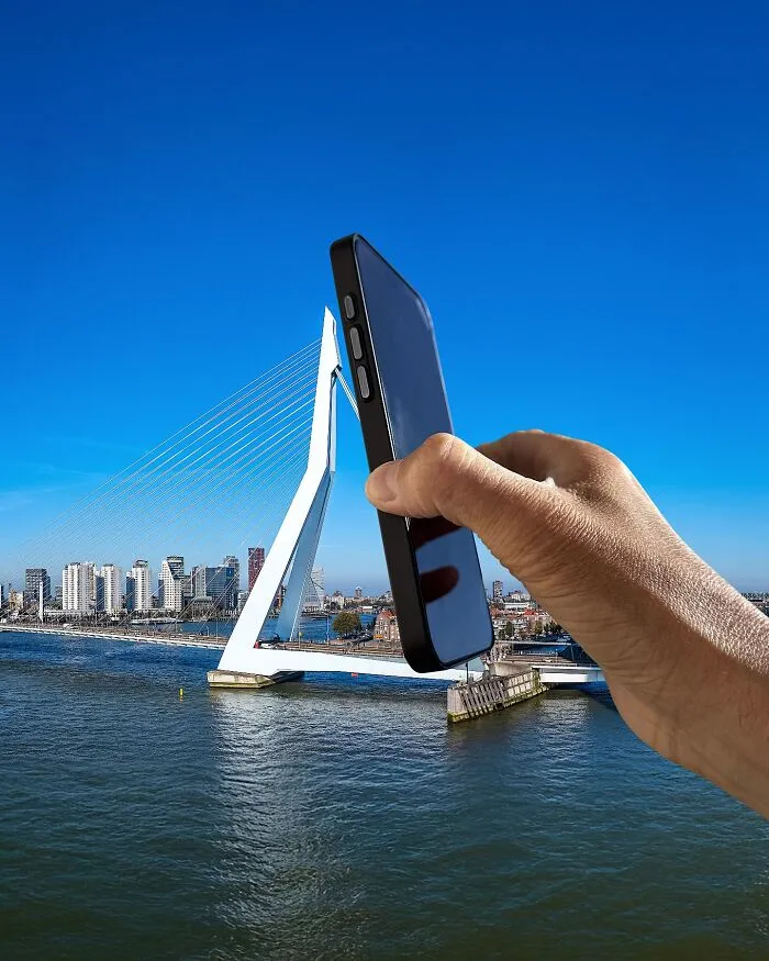 A hand holding a smartphone up to the Erasmus Bridge in Rotterdam, Netherlands, as a clever photo manipulation.
