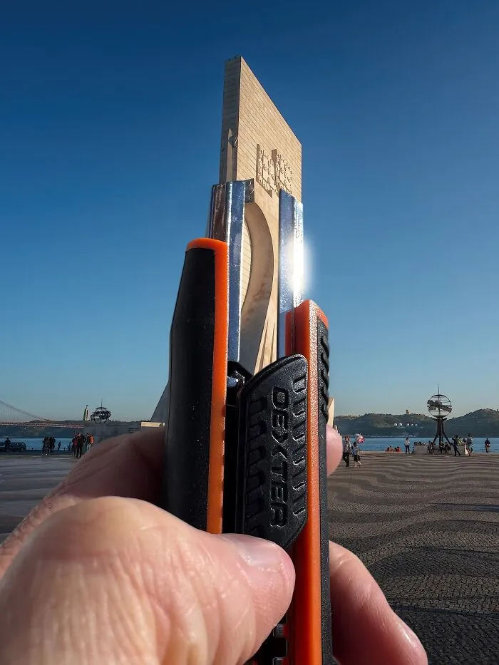 A hand holding a utility knife, aligning it with a tall, modern building. This photo manipulation makes simple objects look like parts of cities.