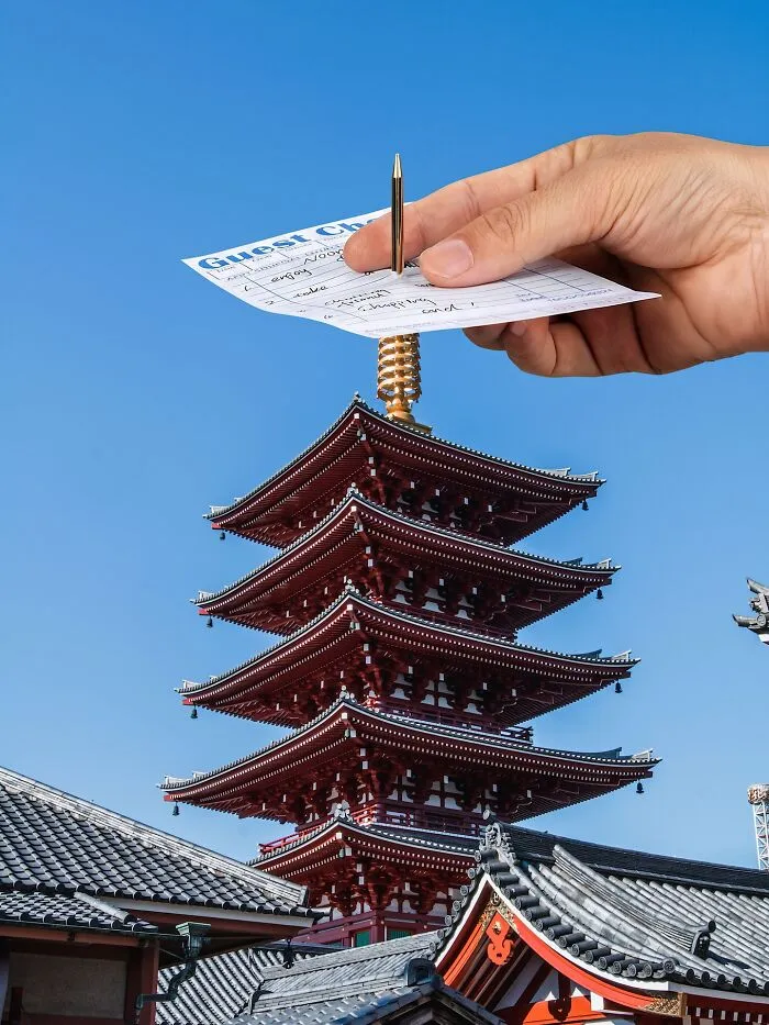 A hand holds a guest check on a spire of a pagoda, a clever photo manipulation making it look like part of a city.