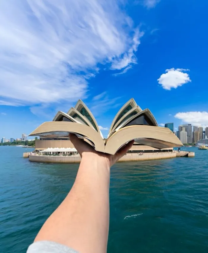 A hand holds an open book in front of the Sydney Opera House, a clever photo manipulation looking like part of a city.