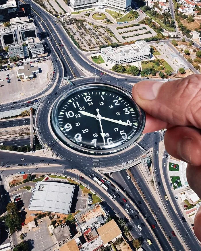 A hand holds a clock over a city roundabout, making it a clever photo manipulation looking like part of the city.