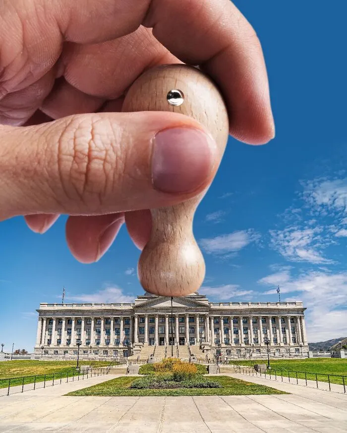 A photo manipulation of a hand holding a wooden stamp, positioning it to look like it's part of a city building.