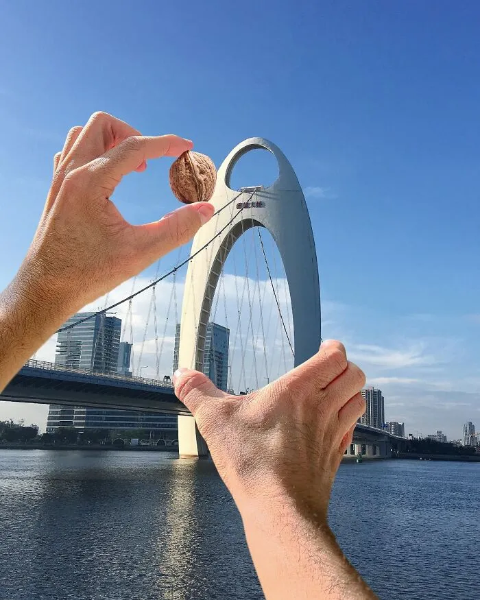 A photo manipulation of hands holding a walnut to look like it's the top of a bridge, making simple objects part of a city.