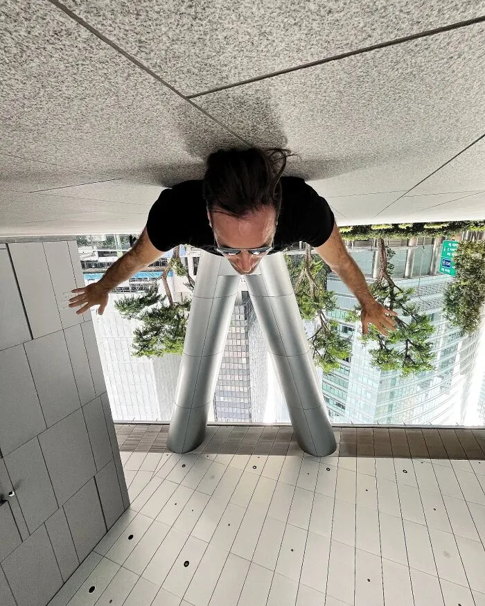 A photo manipulation of a man upside down on a ceiling, with his legs appearing as parts of a city's architecture.