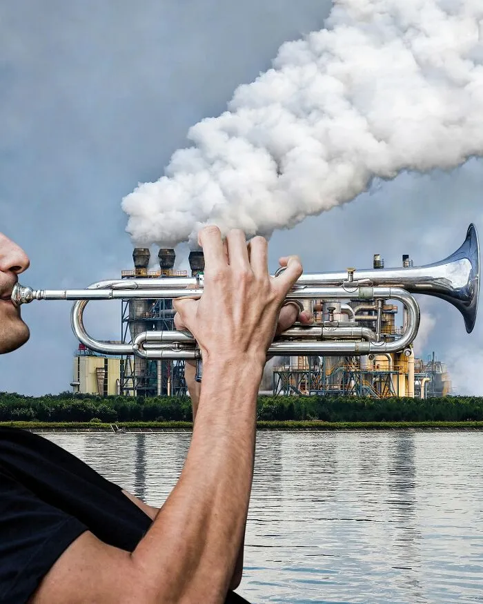 A photo manipulation of a person playing a trumpet, with a factory chimney in the background emitting smoke that looks like it's coming from the trumpet.
