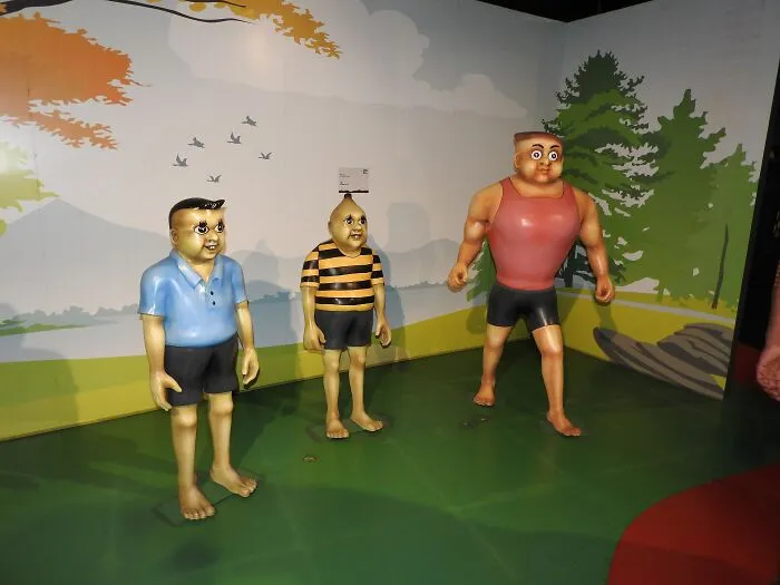 Cartoonish wax figures of three characters displayed in a colorful backdrop of celebrity wax figures