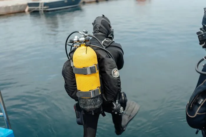 A diver in a black wetsuit with a bright yellow oxygen tank, about to enter the water. Disturbing death stories.