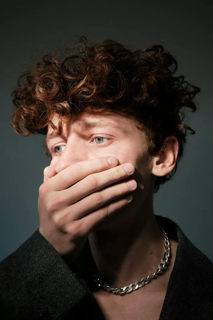 A young person with curly brown hair covers their mouth, looking away with wide blue eyes. Disturbing death stories.