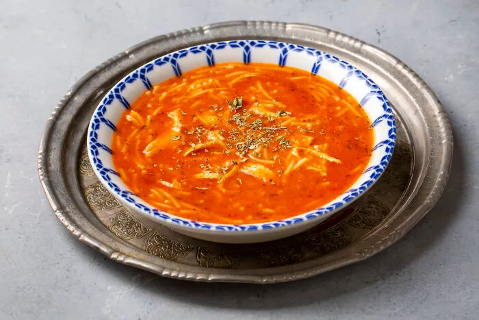Tomato soup with noodles served in a patterned bowl as an affordable poverty meal