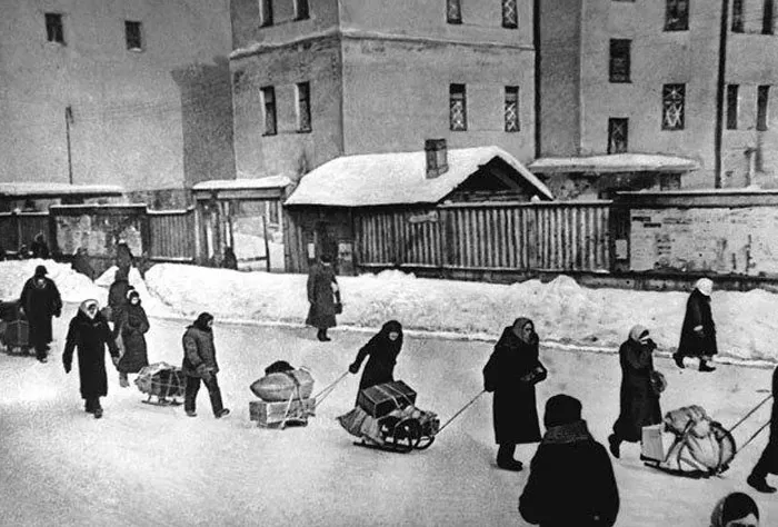 Black and white photo of people in winter pulling sleds with heavy loads in dystopian setting