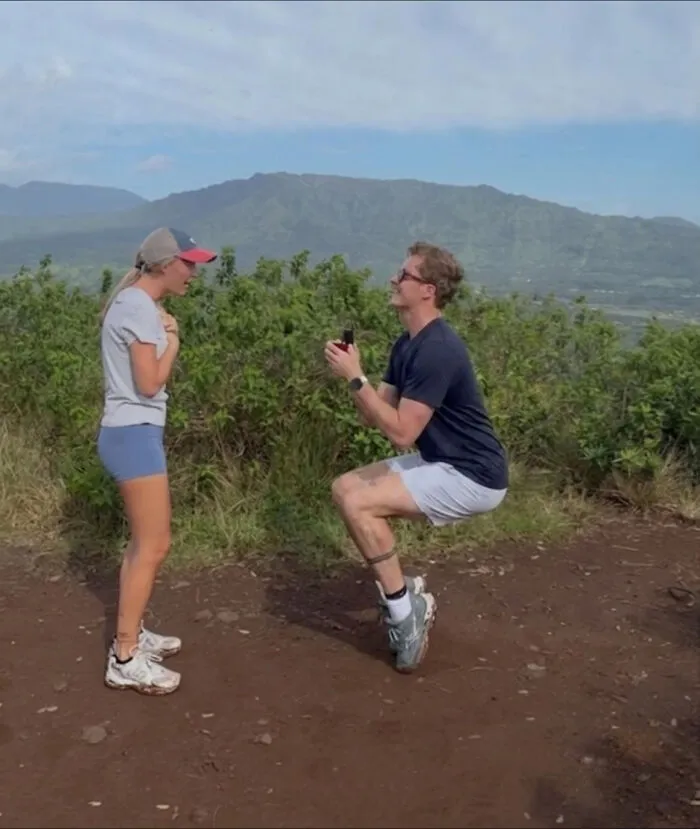 Man proposing to a woman outdoors with mountains in the background, inspiring hilarious edits.