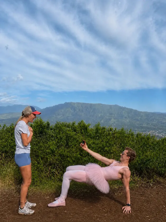 Man in a pink tutu and tights proposes to a woman who looks surprised. A hilarious proposal pic with mountains in background.