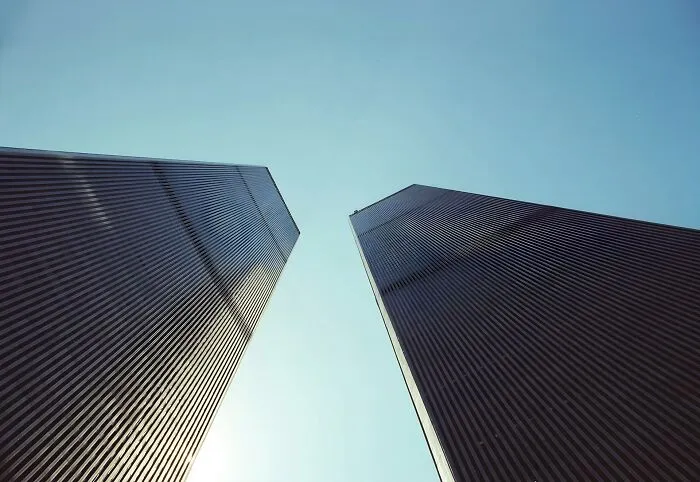 Two dark, imposing skyscrapers rise towards a clear blue sky, evoking a disturbing death story.