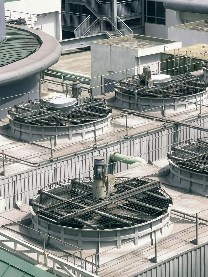 An aerial view of an industrial rooftop with multiple large cooling towers, steel pipes, and stairs. Disturbing death stories.