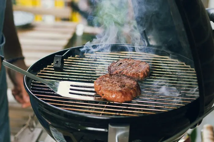 Close-up of burgers grilling on barbecue with smoke rising