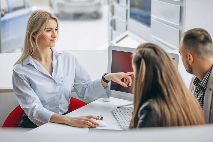 A professional woman pointing at a computer screen to a couple, sharing facts and expertise.