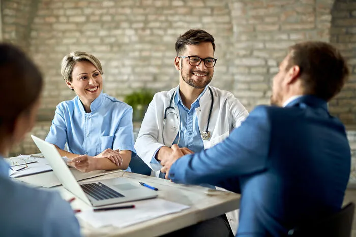 A male doctor in glasses shaking hands with a businessman, a female professional smiling, discussing fun facts.