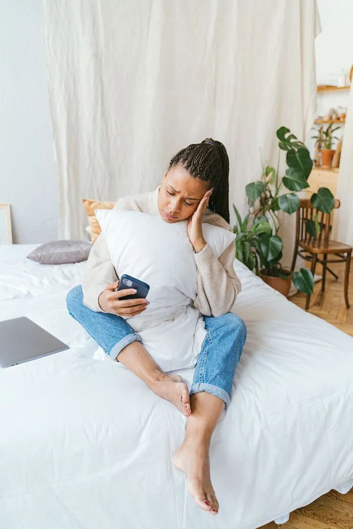 Woman looks upset hugging pillow while checking phone showing exes unhinged posts