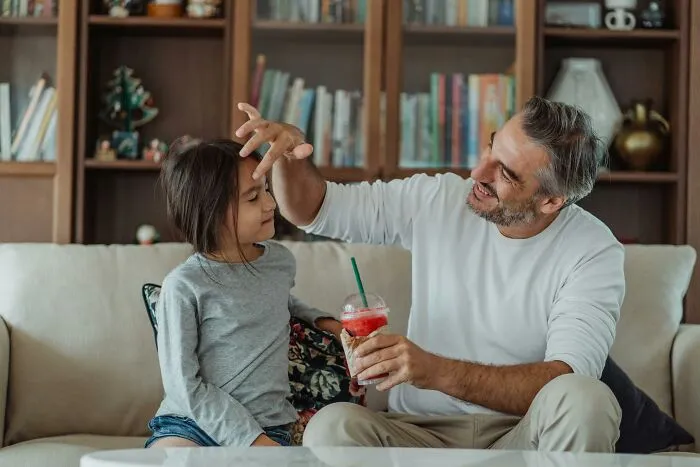 Father playfully interacting with daughter while holding a drink indoors
