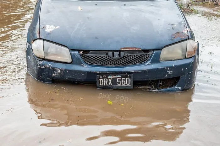 A submerged blue car in muddy floodwaters. The damaged vehicle is half-submerged, reflecting the disturbing death stories of natural disasters.