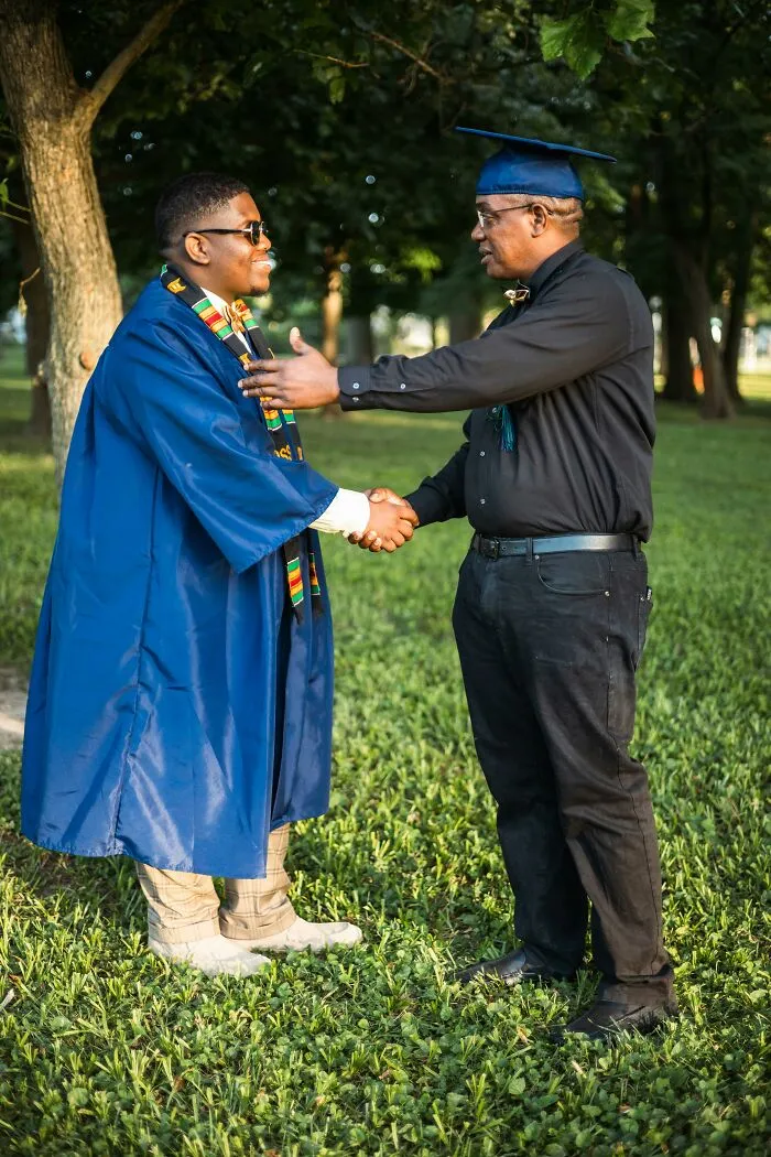 Father congratulating son in graduation gown outdoors celebrating achievement