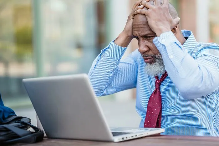 Older generations: Frustrated man with hands on head, looking at laptop. He's struggling to understand Gen Z.