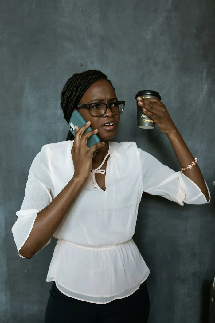 Woman talking on phone holding up a paper coffee cup looking frustrated