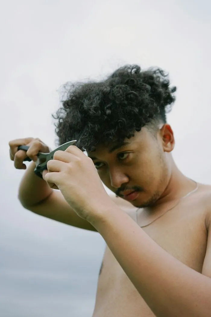 A man with curly hair cutting his own hair, reflecting unexpected wedding drama.