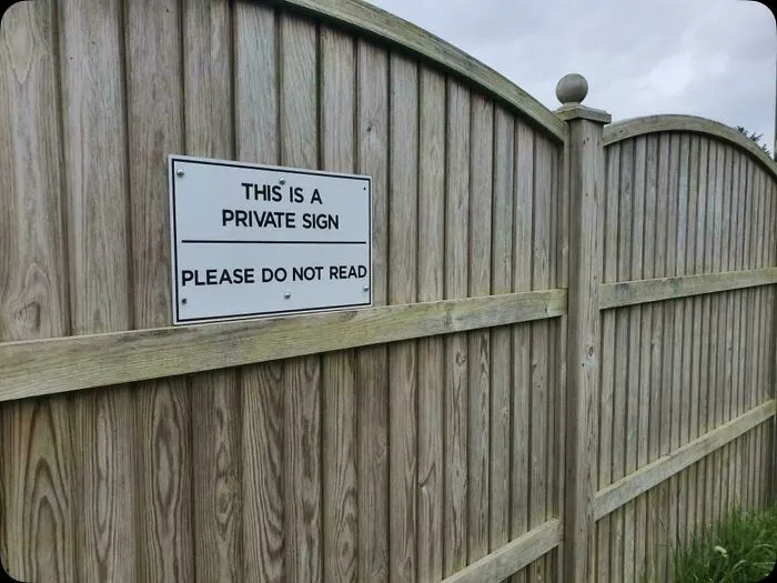 Amusing private sign on wooden fence with contradictory message