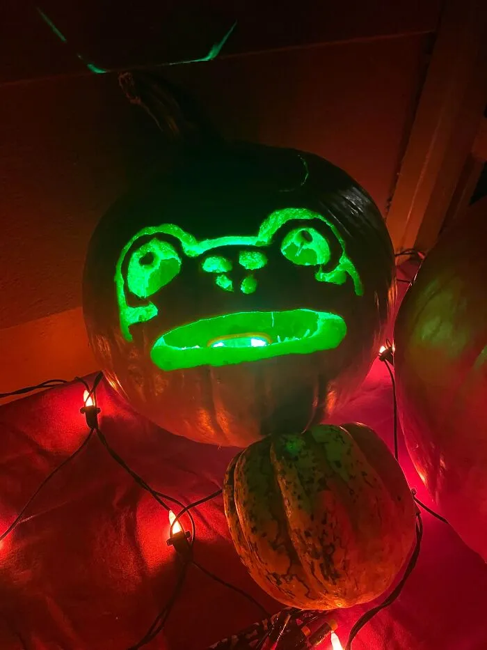 Pumpkin carved with a glowing green frog face surrounded by decorative lights