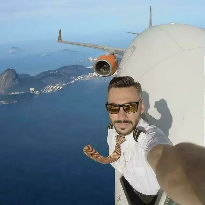 Pilot taking a selfie outside airplane attached to the engine in flight