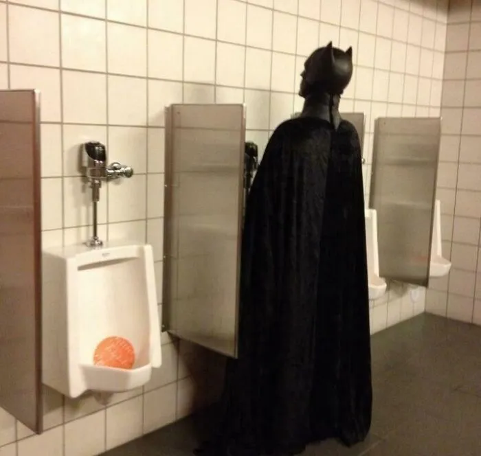 Hilarious person dressed as Batman using a urinal