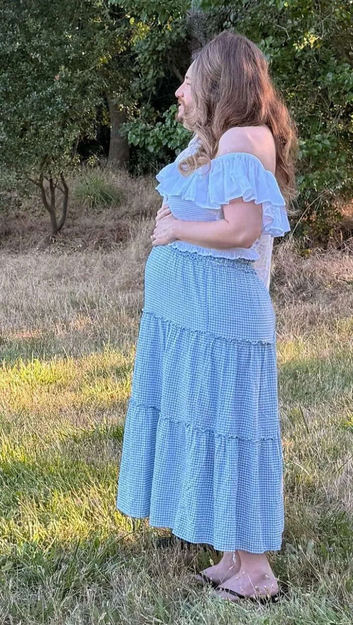 Pregnant person in blue dress standing outdoors in a grassy area