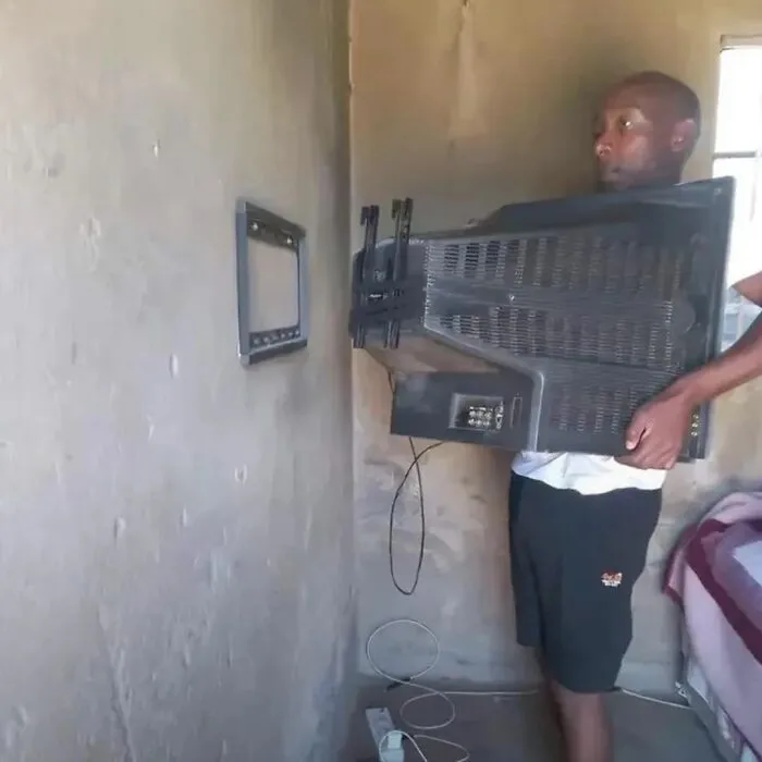 Man struggling to mount a large TV onto a wall bracket in small room