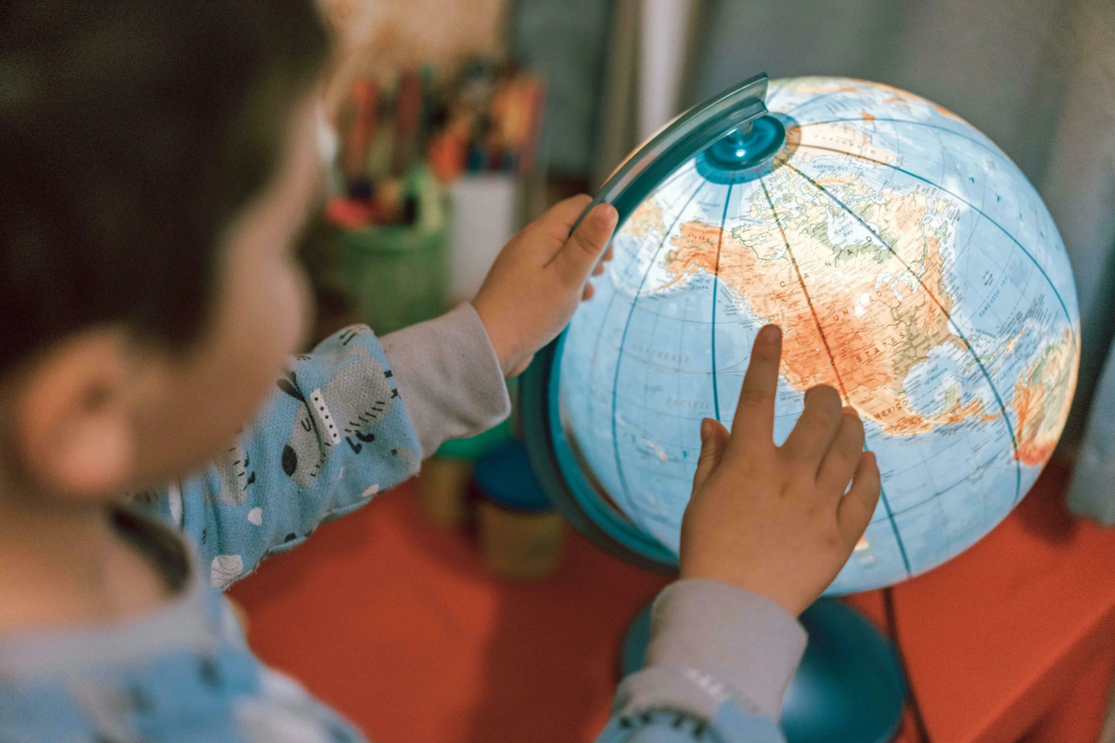 A child's hands exploring an illuminated globe, pointing at North America. General Knowledge Quiz: Europe Questions.