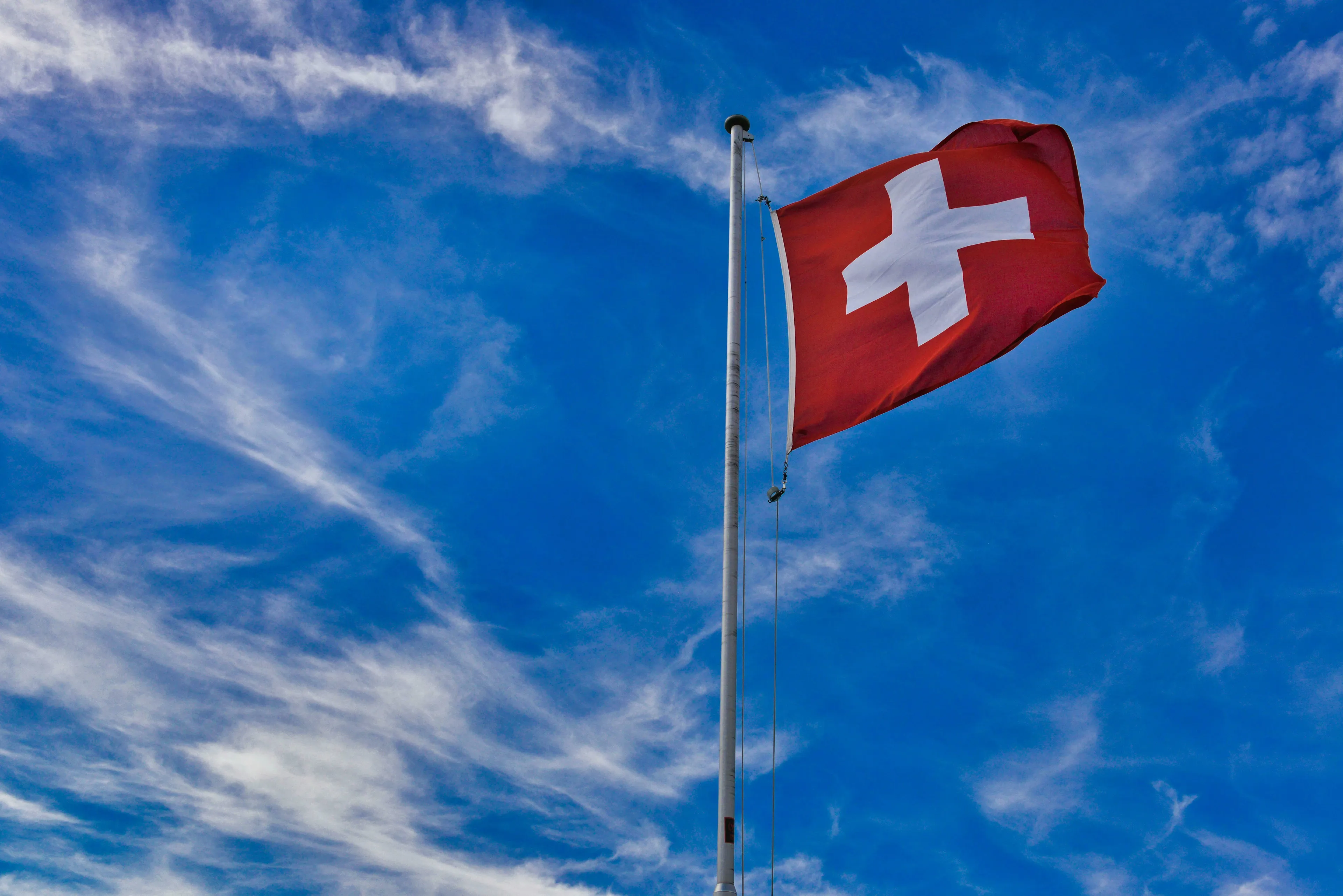 Swiss flag waving against a bright blue sky with wispy clouds. A General Knowledge Quiz: Europe Questions.