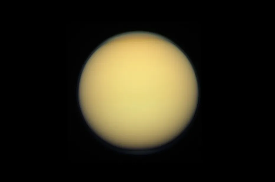 Titan, a moon with a hazy, yellow-orange atmosphere, appearing as a full disc against the blackness of space.