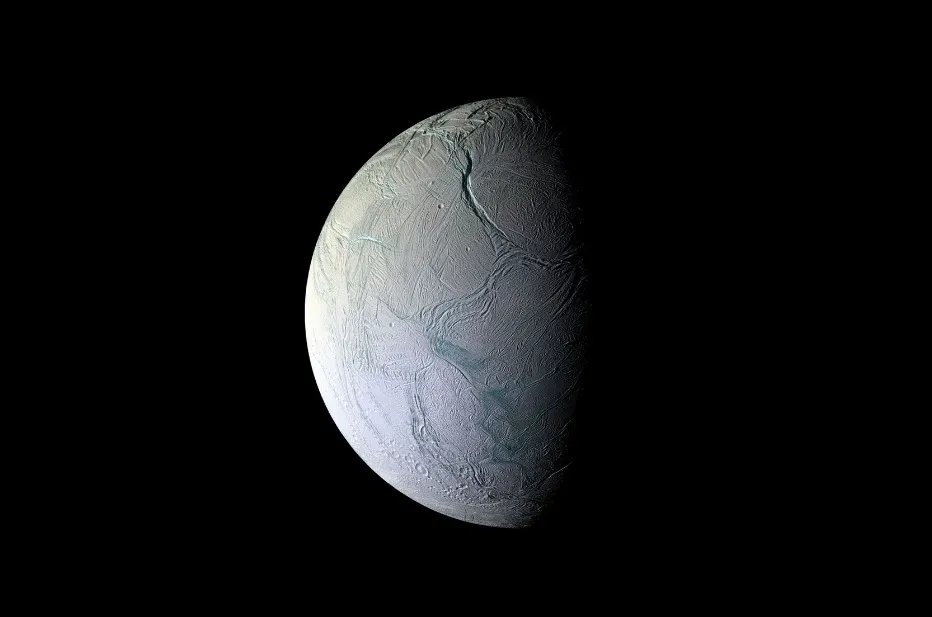 Enceladus, a moon with a cracked icy surface, partially illuminated against the darkness of space, showing its subsurface ocean.