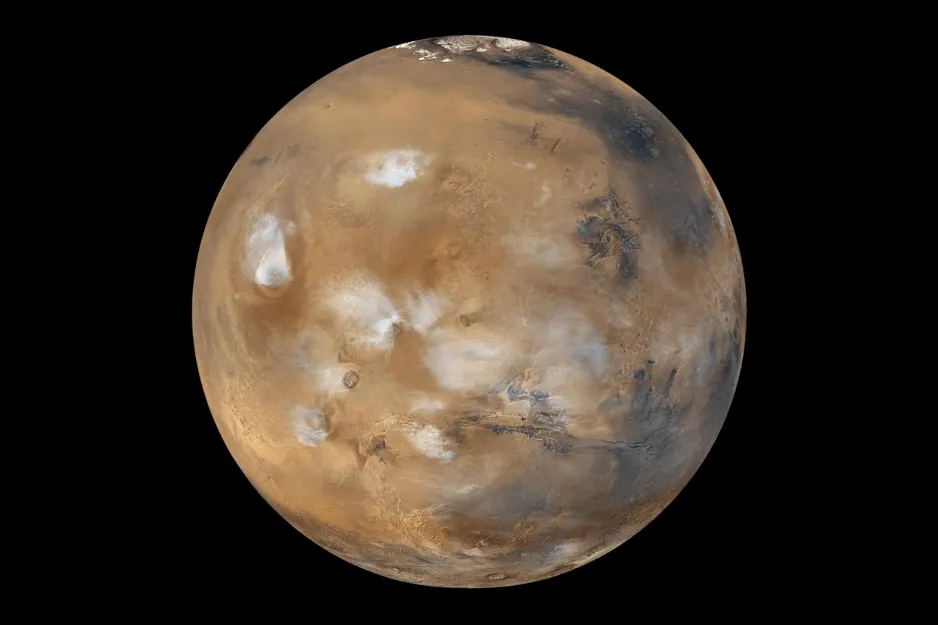 A detailed view of the planet Mars, showcasing its reddish-brown surface with white polar ice caps and cloudy atmosphere.