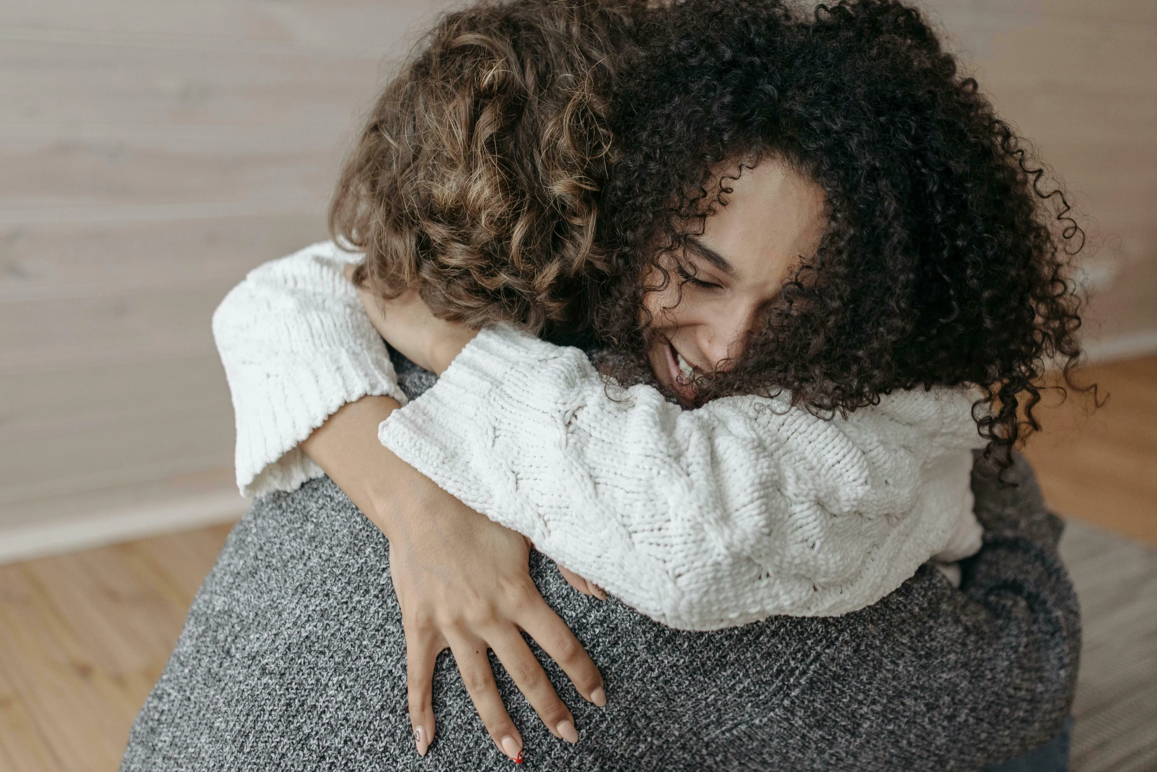 A woman with curly hair, in a white sweater, smiling while hugging someone, depicting forgiveness and handling being wrong.