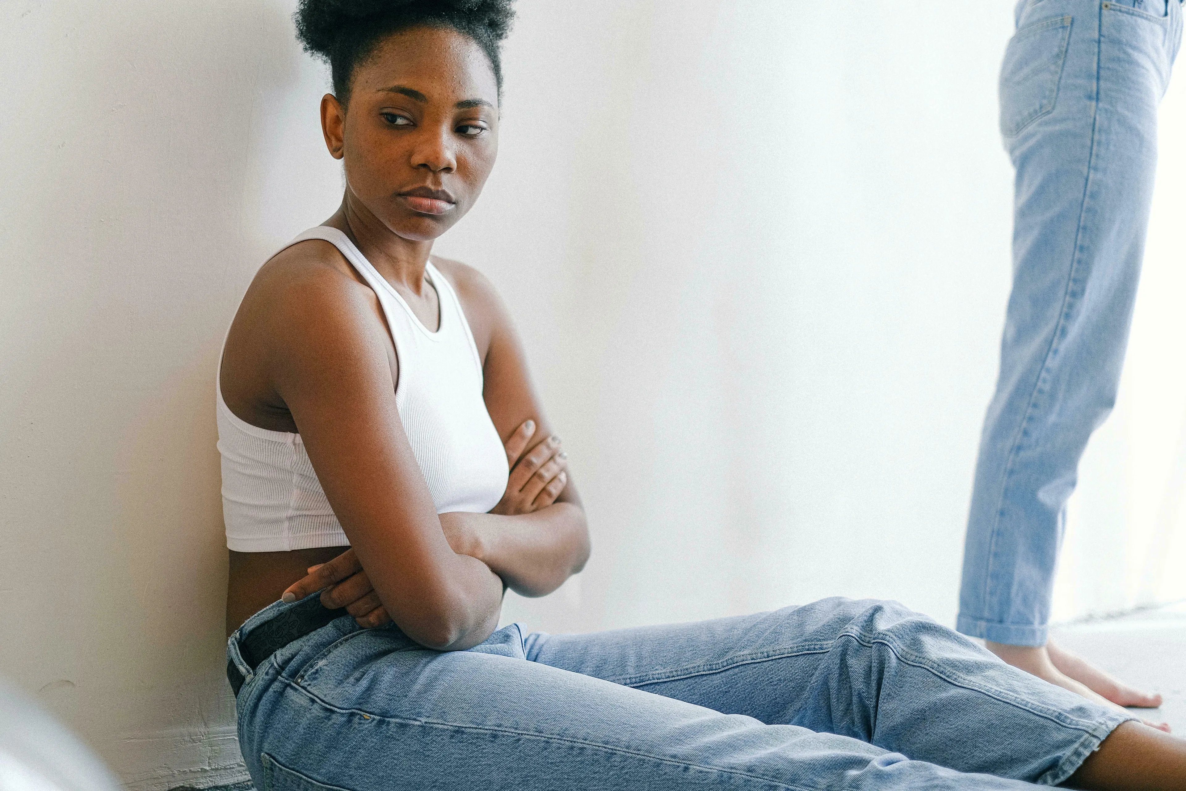 A woman in a white top and jeans with crossed arms, looking away, reflecting on being wrong.