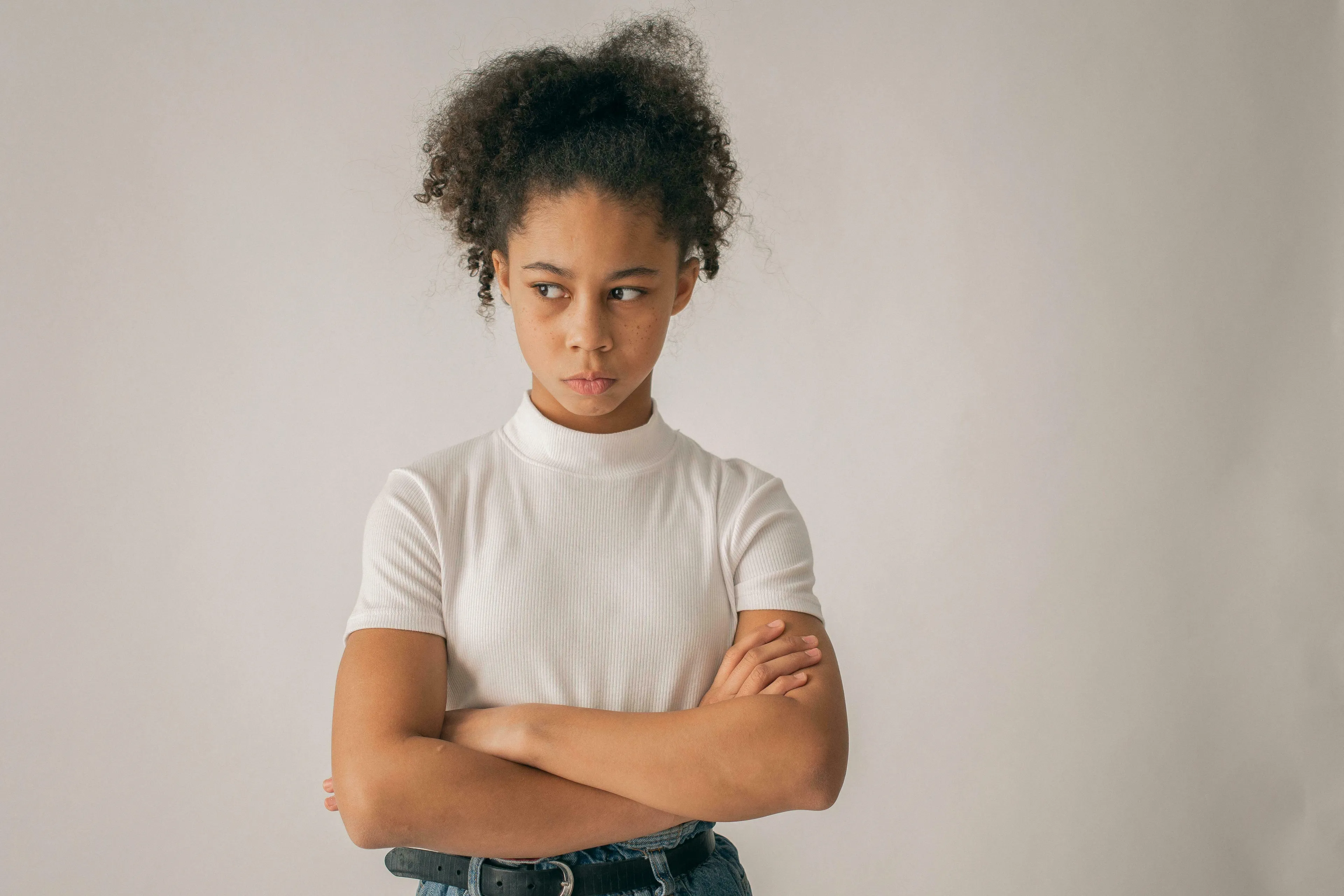 A young girl with curly hair, arms crossed and a serious expression, pondering how to handle being wrong.