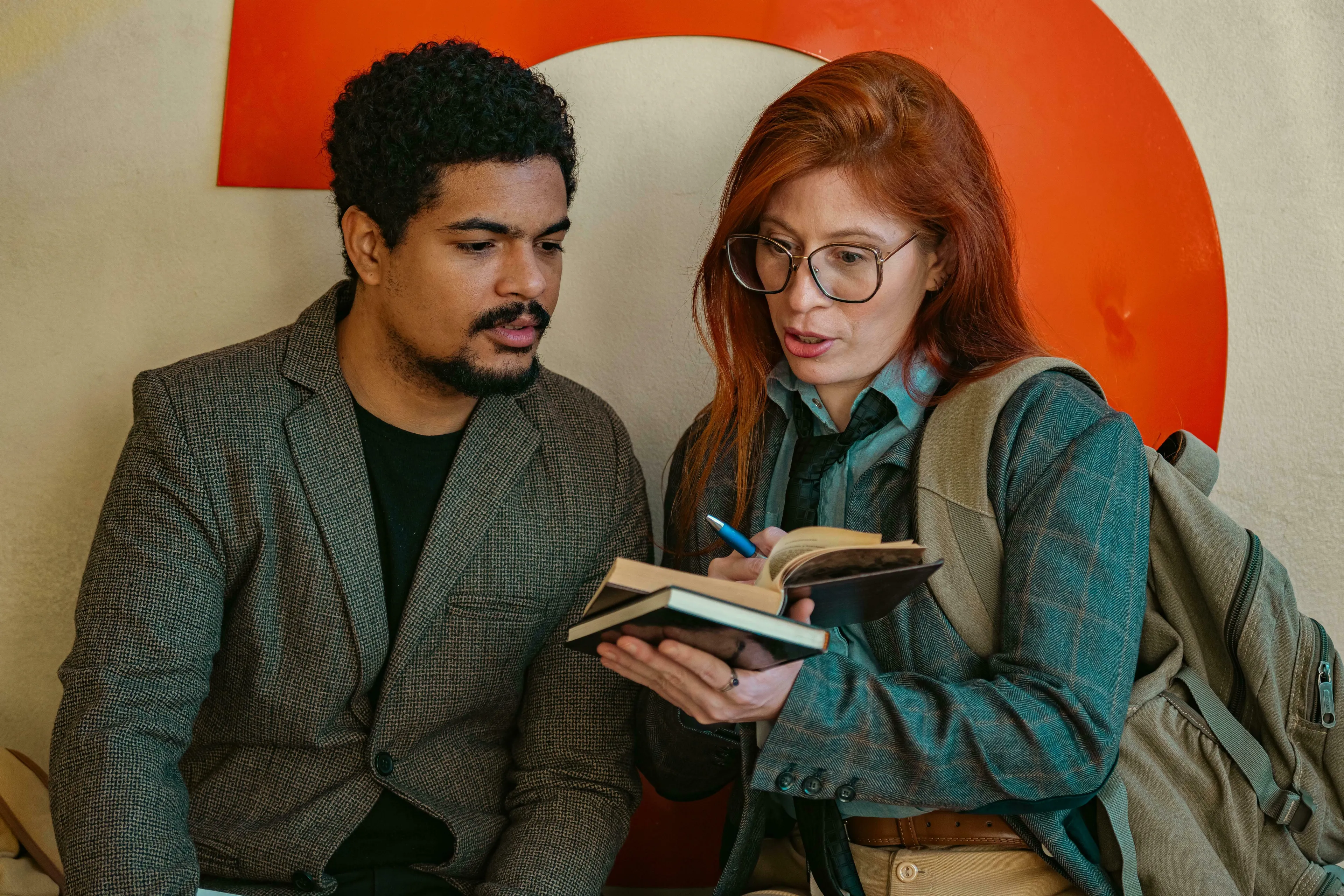 A woman with glasses and red hair is writing in a notebook while a man listens intently. How do you handle being wrong?