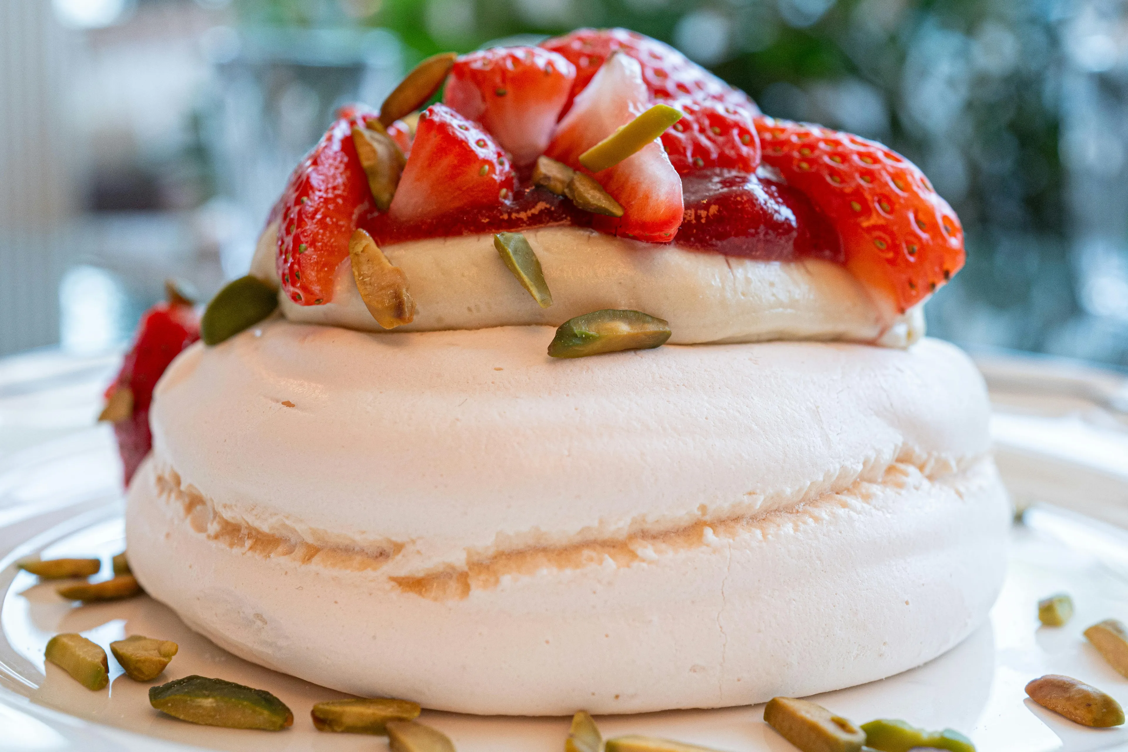 A delightful pavlova dessert topped with whipped cream, fresh strawberries, and pistachios.