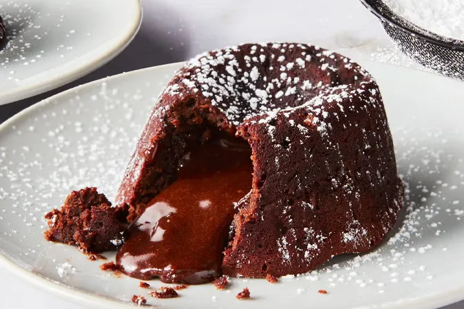 Decadent lava cake on a gray plate, dusted with powdered sugar and rich, molten chocolate oozing from the center.
