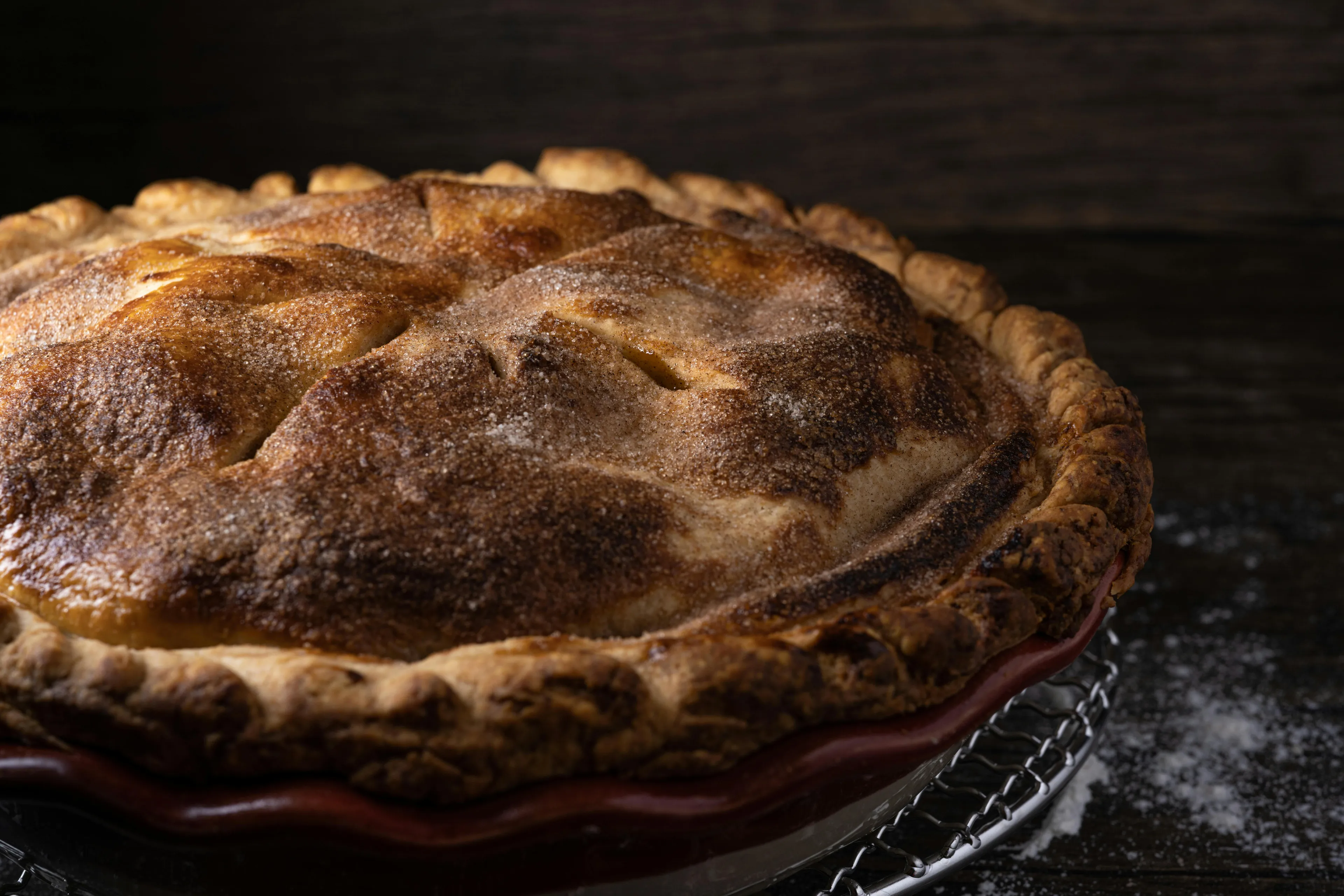 A perfectly baked apple pie, glistening with sugar and cinnamon on its golden-brown crust, sitting in a red pie dish.