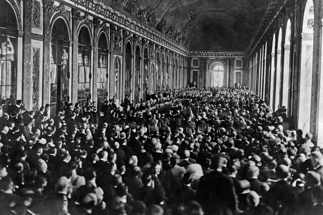 Black and white photo of a crowded hall, depicting the signing of the Treaty of Versailles, a famous historical event.