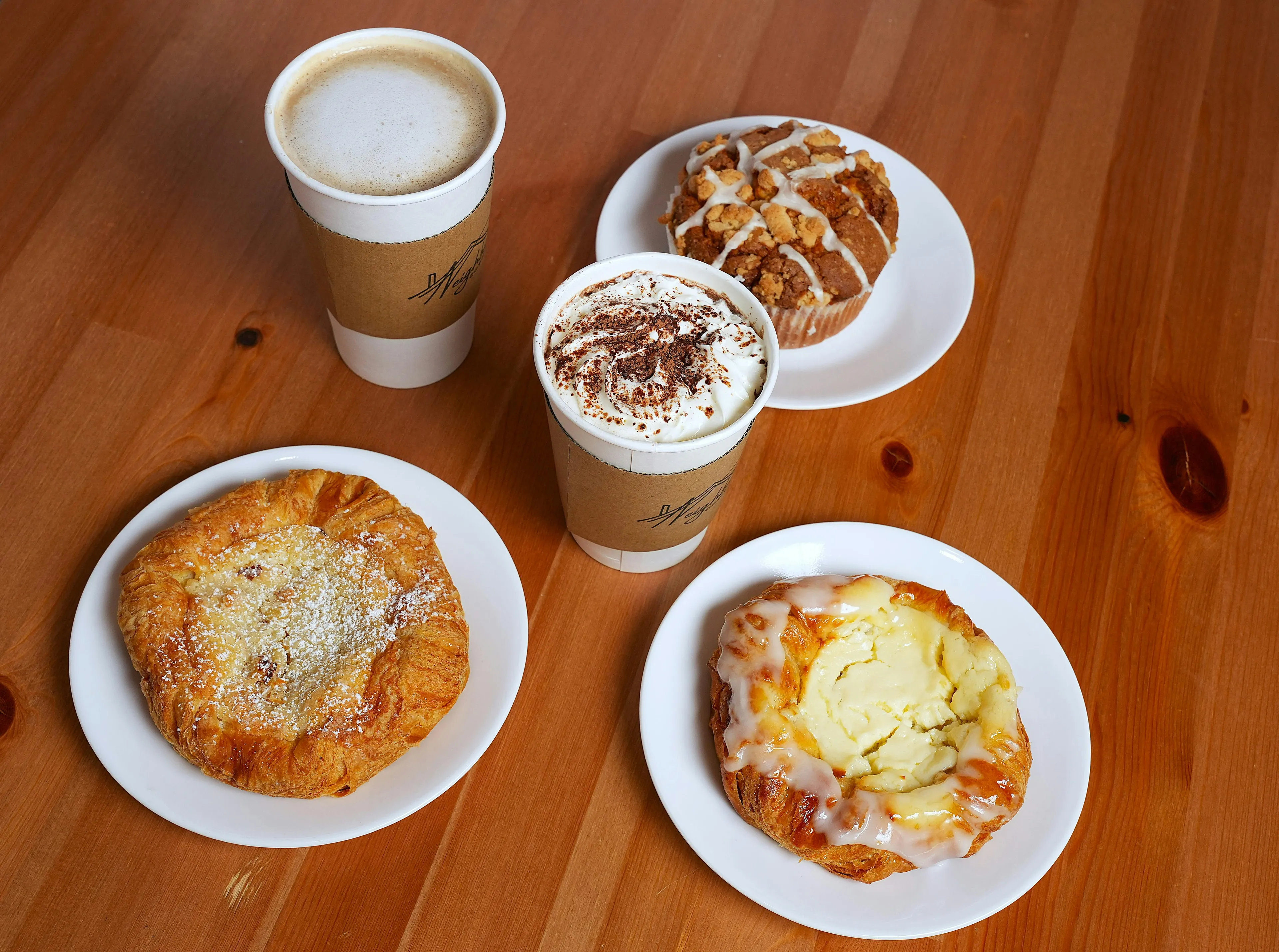 Enjoy a Sunday morning with coffee and fresh pastry. An overhead shot of two coffees and four pastries on a wooden table.