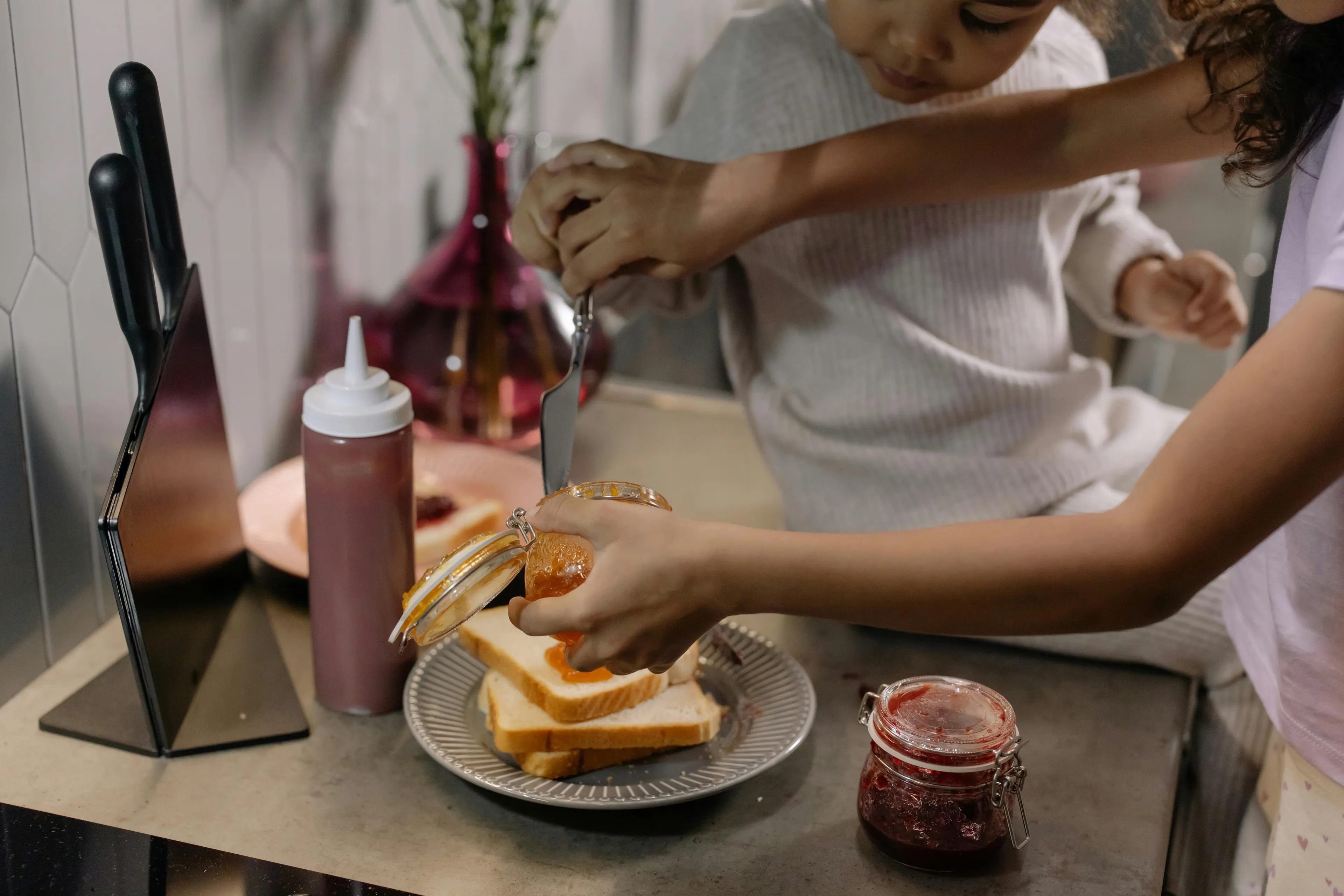 Two children making a big breakfast on a Sunday morning, spreading jam on toast.
