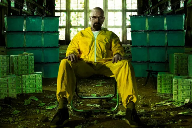 Walter White from Breaking Bad, in a yellow hazmat suit, surrounded by stacks of money and green containers.